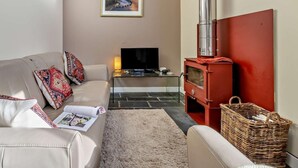 Een woonkamer met een bank, een televisie, een rode houtkachel en een lijst met een afbeelding aan de muur.