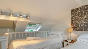 Een slaapkamer met dakraam, nachtkastje met lamp en een behang met patroon.