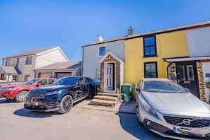 Una calle residencial con coches aparcados, incluyendo un Range Rover y un Volvo, y casas con estilos arquitectónicos variados.