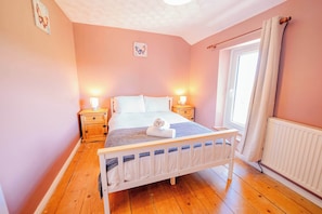 Un dormitorio con cama de madera, mesitas de noche, una ventana con cortinas y un radiador.