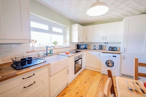 Una cocina moderna con armarios blancos, encimera de madera, lavadora y ventana que deja entrar luz natural.