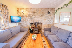 Una sala de estar acogedora con una pared de piedra, una chimenea, dos sofás grises, una mesa de centro de madera y un televisor en la pared izquierda.