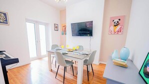 Un comedor con una mesa preparada para cuatro personas, un televisor montado en la pared y un piano en la esquina.