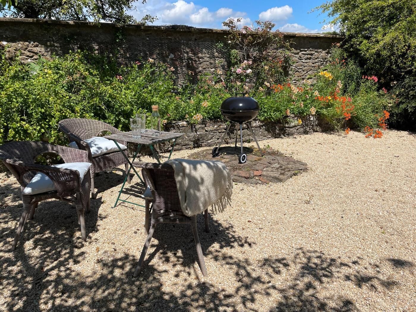 En terrasse med fletningsmøbler, grill og en stenvæg.