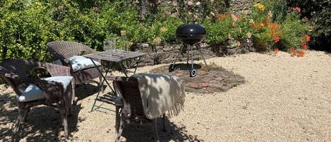 En terrasse med fletningsmøbler, grill og en stenvæg.