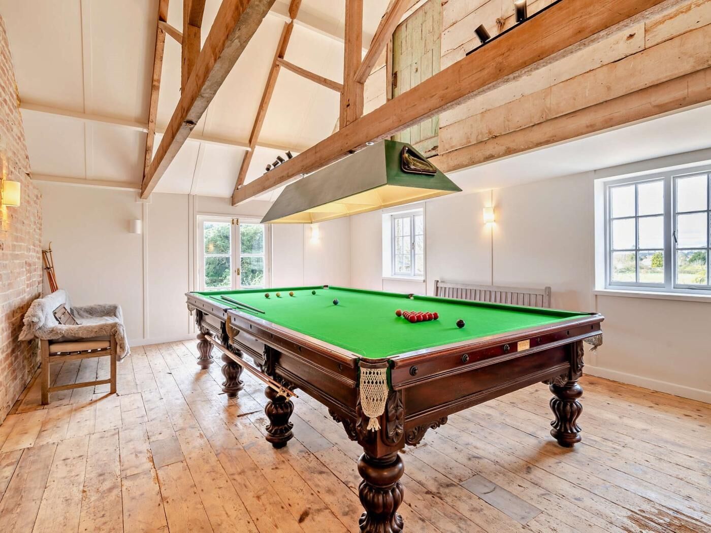 A pool table in a room with wooden beams, a window, and a bench.