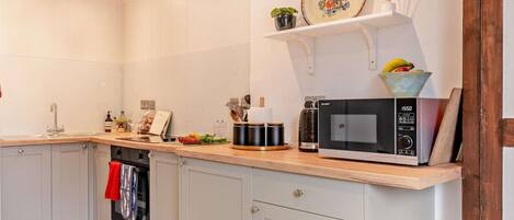 Une cuisine moderne avec des meubles blancs, un four à micro-ondes et une petite étagère ornée d’objets décoratifs.