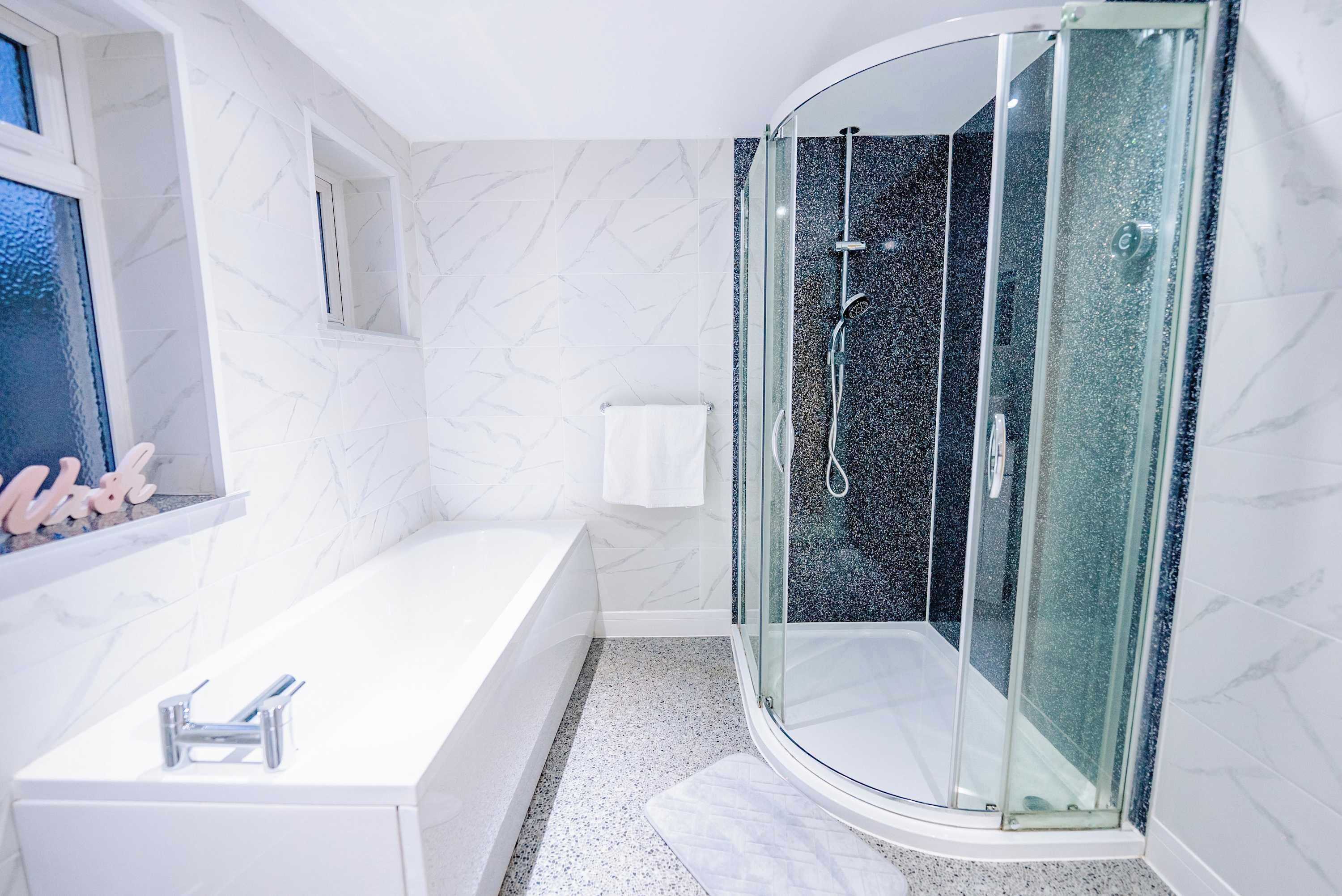 A modern bathroom with a glass-enclosed shower, a white bathtub, and a marble wall.