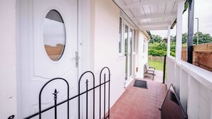 Eine überdachte Veranda mit einer weißen Tür, einer kleinen Sitzecke und Blick auf den Garten.