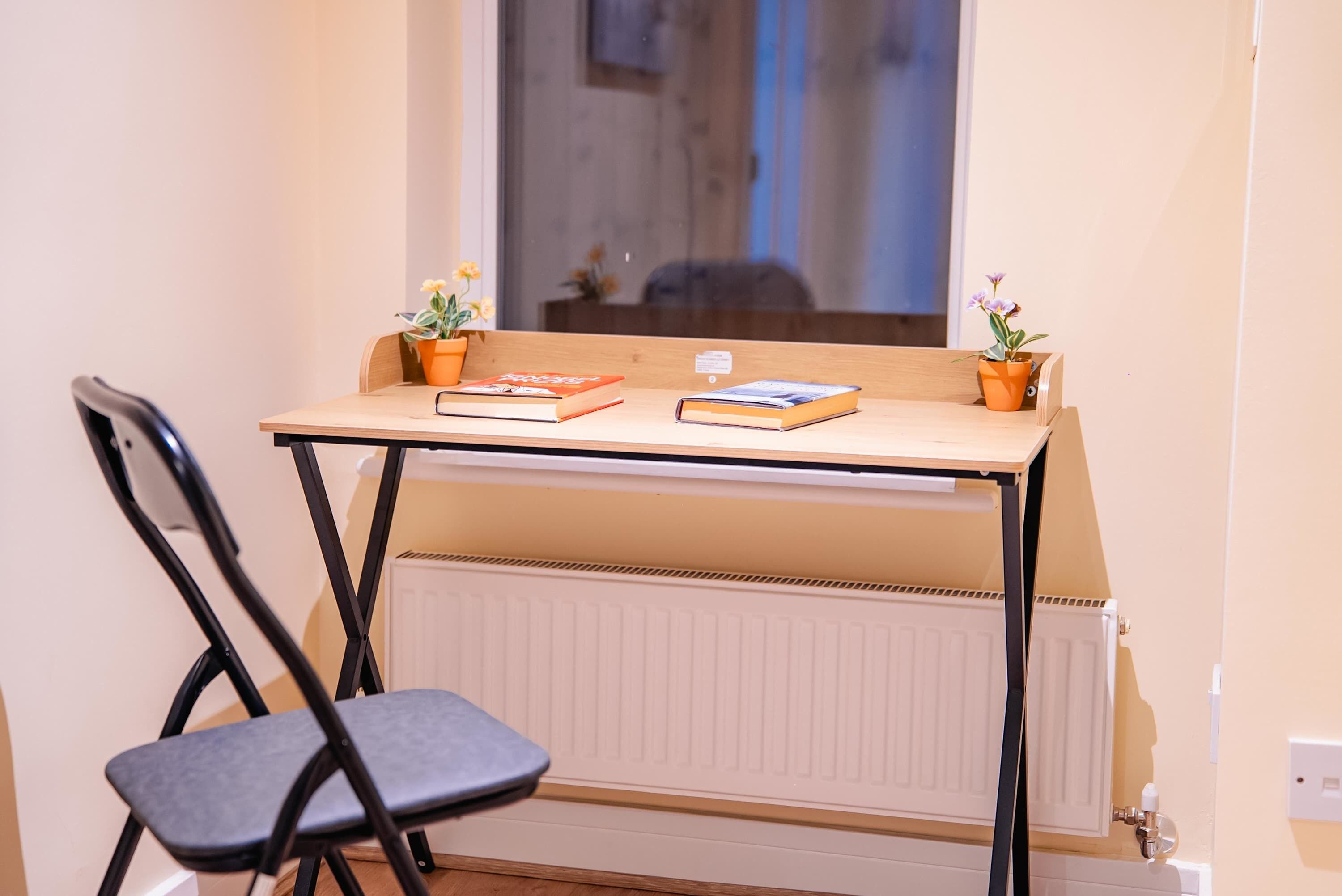 A small study area with a desk, two chairs, two potted plants, and two books.