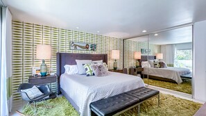 Ein modernes Schlafzimmer mit einem großen Bett, einer Bank, einem Nachttisch, einem Spiegel und einer Wand mit Muster.
