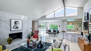 Amplia sala de estar con chimenea, comedor y cocina con ventanas grandes.