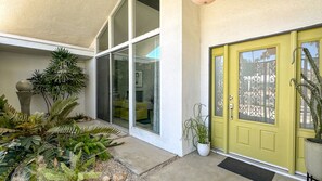 A house with a yellow door, a sliding glass door, and a small garden with various plants.