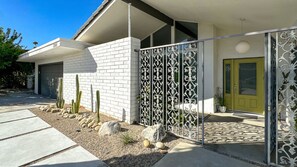 Una casa moderna con fachada de ladrillo blanco, una puerta amarilla y una valla decorativa de metal.