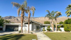 Ein modernes Haus mit Garage, Palmen und einem Berg im Hintergrund.