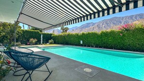 Ein Schwimmbecken mit Bergblick, eine überdachte Terrasse und ein Stuhl.