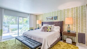 A modern bedroom with a bed, bench, bedside tables, and a view of the outdoors.