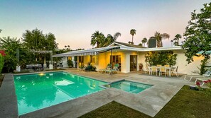 Una casa moderna con piscina, mobiliario exterior y palmeras.