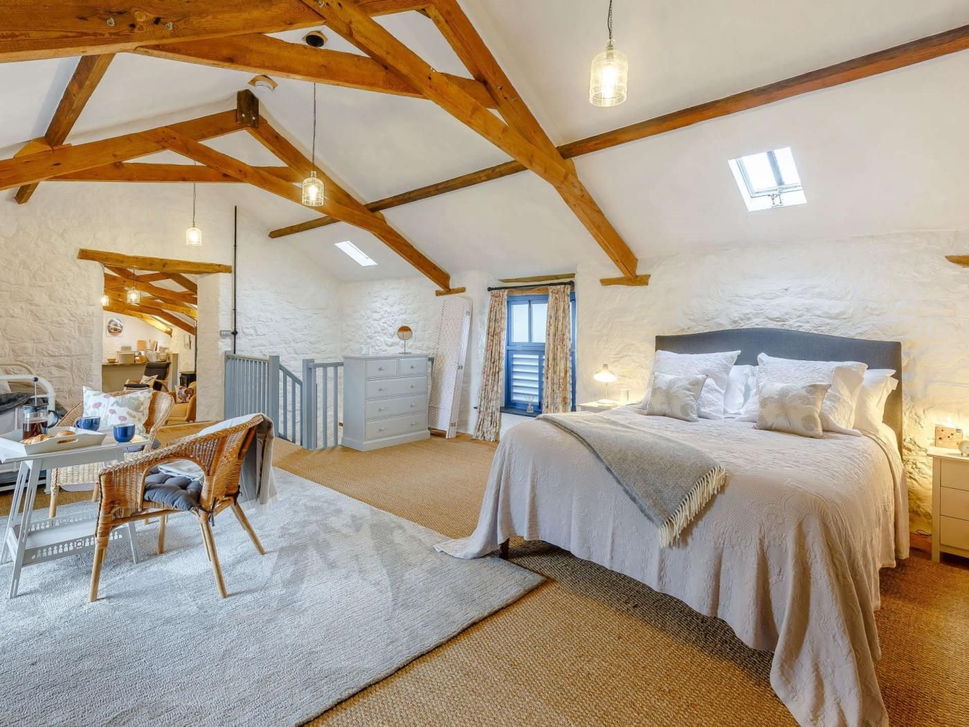 A bedroom with a large bed, a desk with a chair, a dresser, and a window with curtains.