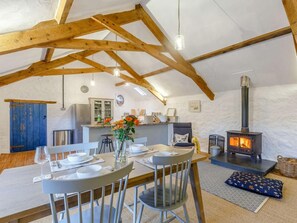 A cozy dining area with a wooden ceiling, a table set for two, and a wood-burning stove in the background.