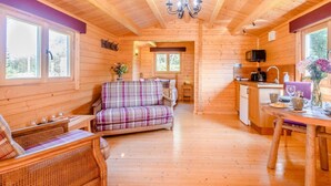 Et sommerhusinteriør med trægulv, en ternet sofa, et spisebord, et tekøkken og en lysekrone.