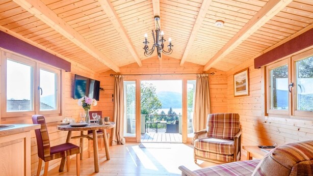 Et interiør af en træhytte med spiseplads, en sofa og en balkon med udsigt.