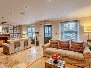 A living room with a fireplace, two sofas, a coffee table with fruit, and framed pictures on the wall. - 3 Bed in Langport (oc-94302) (Curry Rivel)