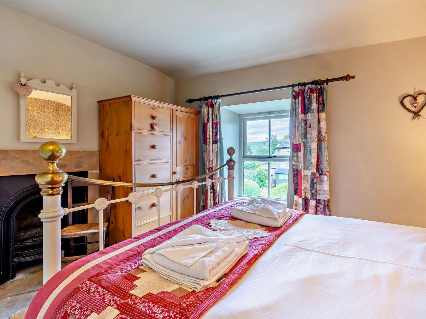 A bedroom with a bed, a wooden wardrobe, a fireplace, and a window with curtains.
