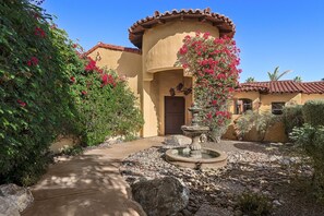 A building with a curved facade, a stone fountain, and a pathway leading to the entrance. - Saltwater Pool/Spa, Tanning Shelf, Firepit, Outdoor Fireplace Shower Free WiFi (Palm Springs)