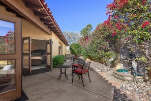 An open patio with a bed, a table, and chairs, surrounded by a garden with a birdcage. - Saltwater Pool/Spa, Tanning Shelf, Firepit, Outdoor Fireplace Shower Free WiFi (Palm Springs)