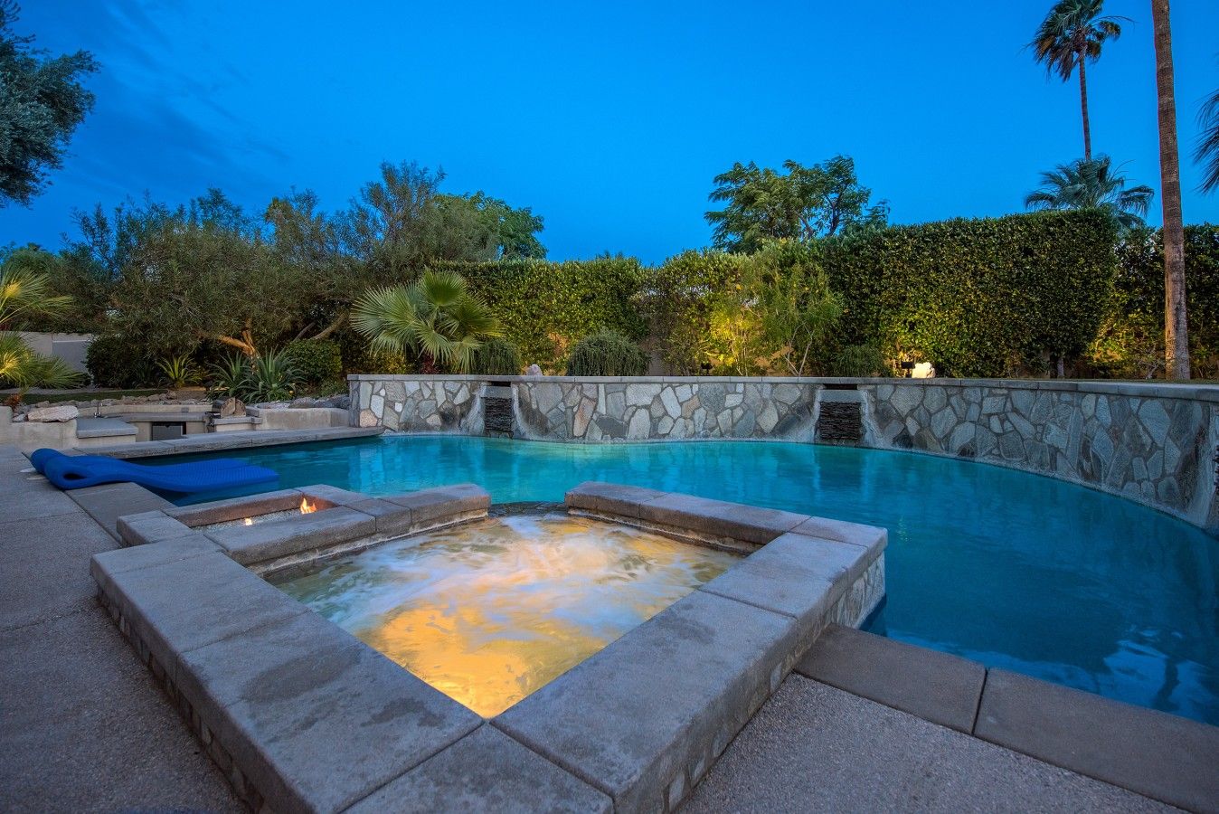 A swimming pool with a stone wall and a hot tub area.