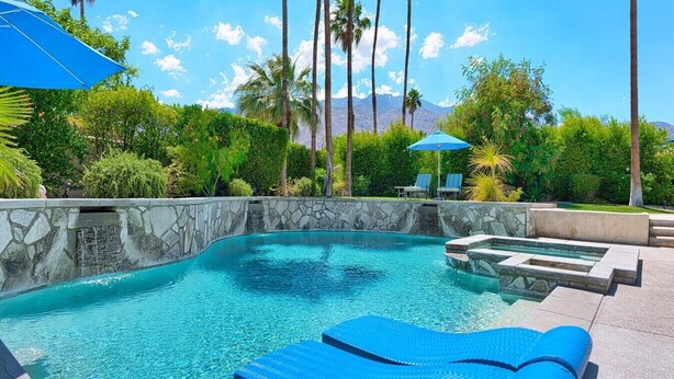 A swimming pool with clear blue water, stone walls, and blue lounge chairs. - Outdoor Shower, Swim-Up Wetbar, Hot Tub, Putting Area, Firepit, EV Charger (Palm Springs)
