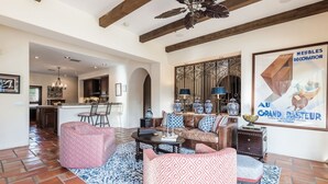 A spacious living area with a fireplace, patterned sofas, and a decorative wall. - Outdoor Shower, Swim-Up Wetbar, Hot Tub, Putting Area, Firepit, EV Charger (Palm Springs)