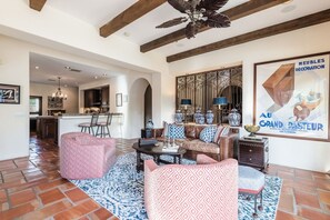 A spacious living area with a fireplace, patterned sofas, and a decorative wall. - Outdoor Shower, Swim-Up Wetbar, Hot Tub, Putting Area, Firepit, EV Charger (Palm Springs)