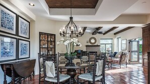 A dining area with a round table, chairs, a chandelier, and patterned wall art. - Outdoor Shower, Swim-Up Wetbar, Hot Tub, Putting Area, Firepit, EV Charger (Palm Springs)