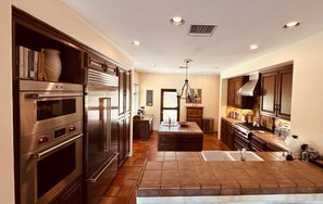 A modern kitchen with built-in appliances, a central island, and a dining area. - Outdoor Shower, Swim-Up Wetbar, Hot Tub, Putting Area, Firepit, EV Charger (Palm Springs)