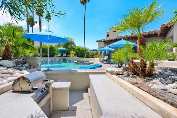 A pool area with lounge chairs, umbrellas, and a grill. - Outdoor Shower, Swim-Up Wetbar, Hot Tub, Putting Area, Firepit, EV Charger (Palm Springs)