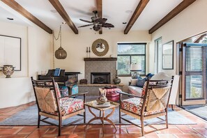 A living room with a fireplace, a ceiling fan, and a piano. - Outdoor Shower, Swim-Up Wetbar, Hot Tub, Putting Area, Firepit, EV Charger (Palm Springs)