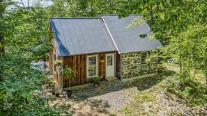 Eine rustikale Holzhütte mit Natursteinfassade, einer Holztür und einem Metalldach, umgeben von dichtem Grün.
