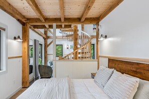 Ein Schlafzimmer mit Holzboden, einem Bett mit weißer Bettwäsche, einem Sessel und Blick auf einen Balkon.