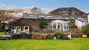 A stone house with a conservatory, surrounded by a fenced garden and a mountain in the background. - 3 Bed in Keswick (oc-94346) (Threlkeld)