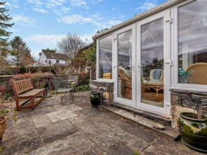 A covered patio with stone flooring, wicker furniture, and a bench. - 3 Bed in Keswick (oc-94346) (Threlkeld)