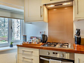 A modern kitchen with a gas stove, oven, and a window with a view of a stone building. - 2 Bed in Bassenthwaite (oc-83287) (Bassenthwaite)
