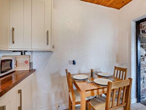 A compact kitchen with white cabinets, a wooden dining table set for two, and a stone wall. - 2 Bed in Bassenthwaite (oc-83287) (Bassenthwaite)