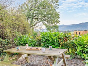 An outdoor wooden table with a tray of food and mugs, surrounded by lush greenery and a view of distant hills. - 2 Bed in Bassenthwaite (oc-83287) (Bassenthwaite)