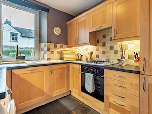 A kitchen with wooden cabinets, a gas stove, a dishwasher, and a window with a view of a house. - 2 Bed in Keswick (oc-94352) (Keswick)