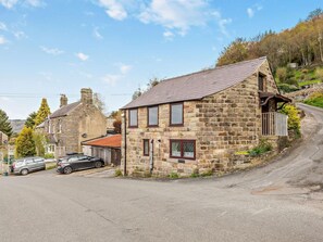 A stone house with a sloped roof, a small porch, and a car parked in front. - 3 Bed in Matlock (oc-pk933) (Hackney)