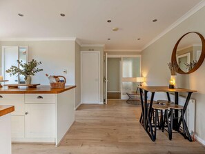 A modern kitchen with wooden cabinets, a dining area with a table and chairs, and a large mirror on the wall. - 5 Bed in Dunbar (oc-94334) (Dunbar)