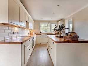 A kitchen with white cabinets, a wooden countertop, a window with a star decoration, and a basket with bread. - 5 Bed in Dunbar (oc-94334) (Dunbar)