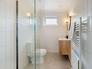 Une salle de bain comprenant des toilettes, un espace de douche vitré, un lavabo avec un meuble-vasque en bois et un porte-serviettes.